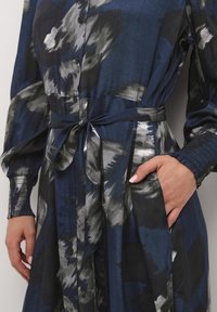 Navyblauwe jurk met knopen, voorzien van een striktaille, lange, wijdvallende mouwen met smockmanchetten en een aquarelprint in grijs en wit.