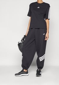 Completo sportivo nero composto da una t-shirt a maniche corte e pantaloni comodi con accenti a strisce bianche e logo. Abbinato a sneaker nere.