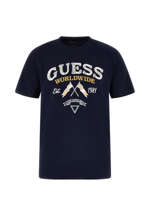 Maglietta blu navy con la scritta "GUESS WORLDWIDE Est. 1981", bandiere incrociate e striscia "LOS ANGELES" con il logo a triangolo sottostante.