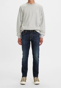 Sudadera gris con cuello redondo, vaqueros azules y zapatillas verde oliva con suelas blancas. Conjunto casual con un ajuste relajado.