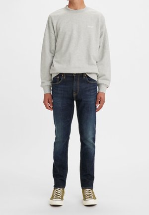 Sweatshirt gris avec un col rond, jean bleu et baskets vert olive avec semelles blanches. Tenue décontractée avec une coupe confortable.