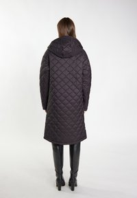 Cappotto nero trapuntato con cappuccio, caratterizzato da un motivo a rombi e un design al ginocchio. Indossato sopra stivali aderenti neri fino al ginocchio.
