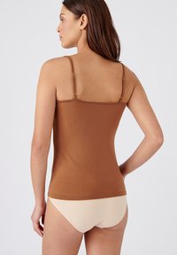 Top aderente marrone con spalline sottili e regolabili, texture liscia e design semplice, abbinato a biancheria intima beige a vita bassa.