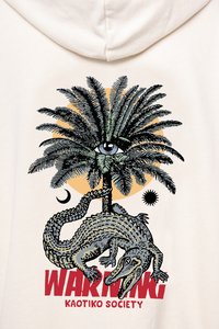 Cremefarbener Hoodie mit einem Palmbaum, einem Auge, einem Krokodil und dem Wort "WARNING" in Rot. Die Illustrationen haben schwarze und grüne Akzente.