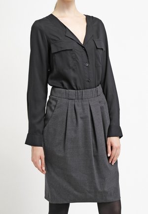 Blouse noire à boutons avec deux poches poitrine, assortie à une jupe plissée gris anthracite. Tissu lisse et coupe ajustée, longueur genoux.