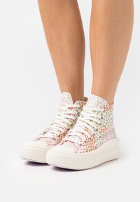 Sneakery za kostkę z białym materiałowym wierzchem, zdobione wielokolorowymi kwiatowymi wzorami i grubą białą gumową podeszwą z textured detailingiem.