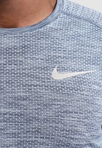 Blå texturerad Nike-idrottströja med rund halsringning och en ljusgrå swoosh-logotyp på bröstet, med ett rutmönster.