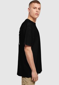 Sort bomulds T-shirt med rund hals, korte ærmer og afslappet pasform, med et grafisk design på fronten og siden.