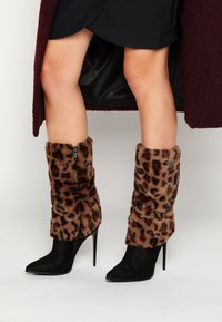 Czarne botki na szpilce z ostrym noskiem, z mankietami z futra w leopardzi wzór i zamkiem błyskawicznym z boku. Gładka tekstura i kontrastowe wzory.