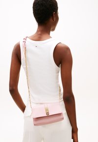 Pink leather crossbody bag with a gold chain strap, featuring a flap closure and smooth surface texture. Accented with a metal clasp.