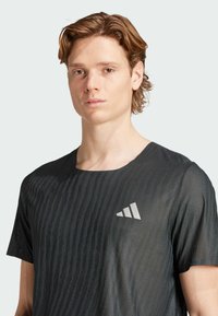 Camiseta atlética negra de tejido ligero con un patrón texturizado, mangas cortas y un logo triangular reflectante en el pecho.