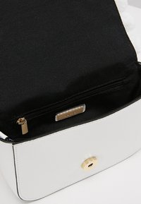 L'interno della borsa in pelle bianca presenta una fodera in tessuto nero, una tasca con zip, accessori in oro e una chiusura magnetica.