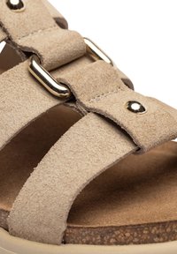 Sandalia de ante beige con correas texturizadas, acentos de hardware dorado y una plantilla de corcho. Presenta un diseño abierto y material suave y duradero.
