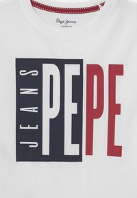 Biała koszulka z nadrukiem z wyraźnymi granatowymi, czerwonymi i białymi literami w stylu block, na których widnieje napis "PEPE JEANS". Okrągły dekolt i teksturowana tkanina.