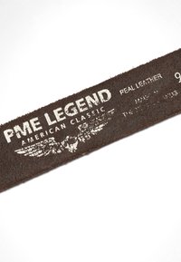 Section d'une ceinture en cuir marron foncé montrant un texte usé en blanc "PME Legend American Classic" et un logo ailé.