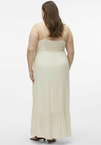 Maxi dress beige chiaro con spalline regolabili, corpetto arricciato e gonna fluente con orlo arricciato. Texture e silhouette morbide.