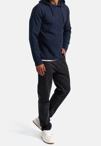 Sudadera de ribete azul marino con cordones ajustables, combinada con jeans negros y zapatillas blancas. Silueta casual y ajustada que enfatiza la comodidad.
