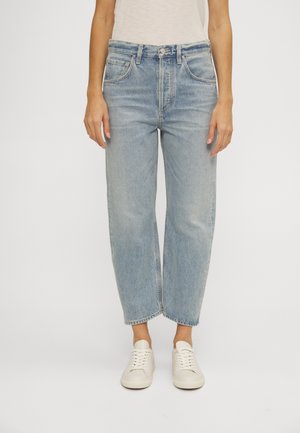 Jeans in denim blu chiaro a vita alta con una vestibilità rilassata, design a gamba dritta, sfumature leggere e cinque tasche. Indossati con scarpe da ginnastica bianche.