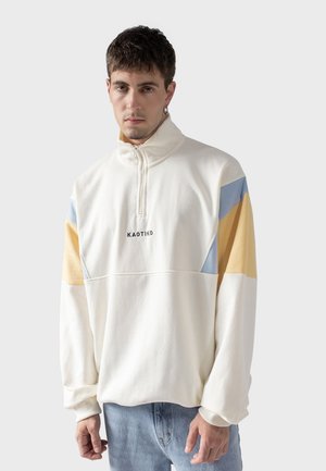 Suéter crema con media cremallera, con paneles en azul, amarillo y blanco. Material de algodón con un corte relajado y bordado de marca.