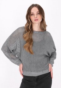 Pull grigio chiaro lavorato a maglia con un design morbido, caratterizzato da una grande trama a rete, maniche ampie e un orlo a coste. Abbinato a jeans scuri.