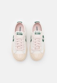 Zapatillas de cuero blancas con acentos en rosa, punta brillante, logo de estrella verde y laterales texturizados. Cuentan con cordones planos y cuellos acolchados.