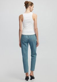 Top de tirantes blanco acanalado combinado con jeans rectos de color azul claro. El conjunto presenta una silueta ajustada y un diseño minimalista. Tacones negros completan el look.