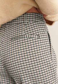 Rutede bukser i houndstooth-mønster med sorte, hvide og brune farver. Har en baglomme og en tætsiddende pasform.