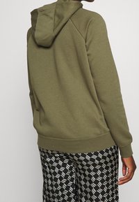 Oliwkowa bluza z kapturem ze sznurkiem, ściągaczami na mankietach i u dołu. Posiada rękawy raglanowe. Połączona z czarnymi spodniami w wzory.