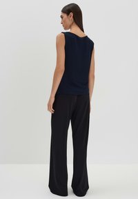 Top senza maniche di colore blu navy con scollatura a barca, abbinato a pantaloni neri a gamba larga, realizzati in un tessuto morbido e liscio con una vestibilità rilassata.
