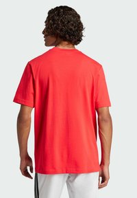 T-shirt in cotone rosso con maniche corte, collo tondo e una parte posteriore semplice. Orlo cucito visibile e una texture liscia.