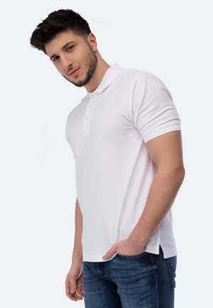 Polo bianco a maniche corte con apertura a due bottoni, vestibilità su misura, fessure laterali e tessuto di cotone liscio. Indossato con jeans blu.