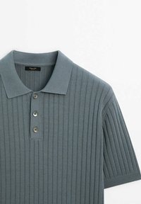 Polo gris côtelé avec un col classique, une patte à trois boutons et des manches courtes, fabriqué à partir d'un tissu doux et texturé.
