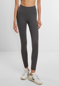 Høyt liv grå ribbede leggings med elastisk stoff, tettsittende design og minimale sømdetaljer, parret med hvite joggesko.