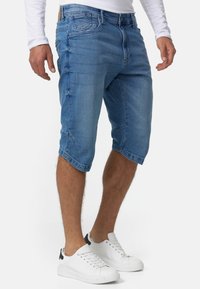 Shorts de mezclilla azul claro con un corte relajado, que presentan un diseño de cinco bolsillos, detalles de costura y puños doblados. Llevados con zapatillas blancas.