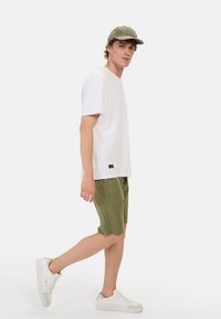 Hvid t-shirt med rund hals paired med olivengrønne shorts, suppleret med en grøn kasket og hvide sneakers. Enkel, afslappet outfit-design.