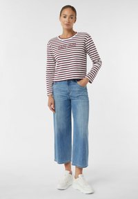 Gestreiftes langärmliges Oberteil in Burgund und Weiß, mit grafischem Text auf der Brust, kombiniert mit hellblauen weiten Jeans und weißen Sneakers.