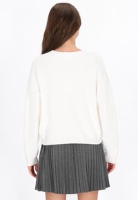 Biały sweter dziergany o luźnym kroju w połączeniu z ciemnoszarym spódnicą plisowaną z pionowymi paskami i warstwowym dołem.