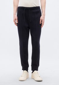 Μπλε σκούρα φόρμα με ελαστική μέση και κορδόνι. Διαθέτει πλαϊνές τσέπες και ριμπ μανσέτες, φτιαγμένη από υφασμάτινο βαμβάκι με υφή.