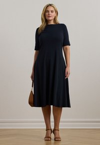 Μπλε ναυτικού χρώματος φόρεμα μέχρι το γόνατο με λεία υφή, κοντά μανίκια και στρογγυλή λαιμόκοψη, συνδυασμένο με καφέ τσάντα χειρός και λουράκια ψηλές γόβες.