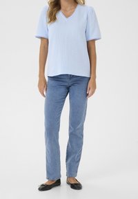 Blusa de manga corta azul claro con escote en V, tejido texturizado y acabado de encaje. Combinada con jeans rectos azul claro y slippers negros.