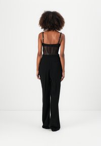 Schwarzer Body mit transparentem Netzpaneel am Rücken, verstellbaren Trägern, kombiniert mit hochgeschnittenen, weiten schwarzen Hosen.
