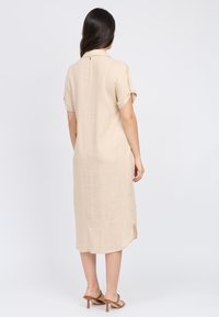 Abito di lino beige con maniche corte arrotolate, dettagli con bottoni sul retro e spacchi laterali, caratterizzato da un design morbido e di lunghezza media.