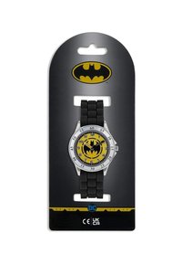 Montre sur le thème de Batman avec un cadran jaune arborant un symbole de chauve-souris, un boîtier en argent et un bracelet en caoutchouc noir. Présentée sur une carte de fond noire.