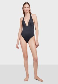 Bañador negro de una pieza con escote en V profundo, tirantes halter y una textura suave. Diseño simple sin patrones ni acentos.