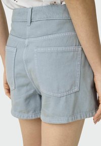 Shorts en jean bleu clair avec une taille haute, deux poches arrière et des détails cousus. Le tissu a une texture lisse.