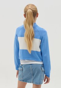 Maglione corto a righe blu e bianche con maniche lunghe, realizzato in materiale lavorato a maglia, abbinato a una gonna di jeans. Texture liscia, design casual.