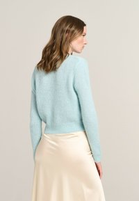 Light blue knitted sweater with a soft texture, fitted shape, long sleeves, and ribbed hem, paired with a cream satin skirt.