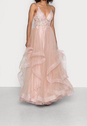 Vrouw draagt een mouwloze, lichtroze jurk met een lijfje van bloemrijke kanten stof en een vloeiende, geruffleerde tule rok.