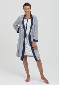 Granatowa i biała w paski długa szata z granatowym kołnierzem, noszona na białej sukience w czarne kropki z zapięciem na guziki.