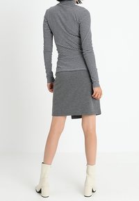 Långärmad randig topp i grått och vitt, ihop med en grå kjol. Modellen bär beige ankelstövlar med kvadratisk klack.